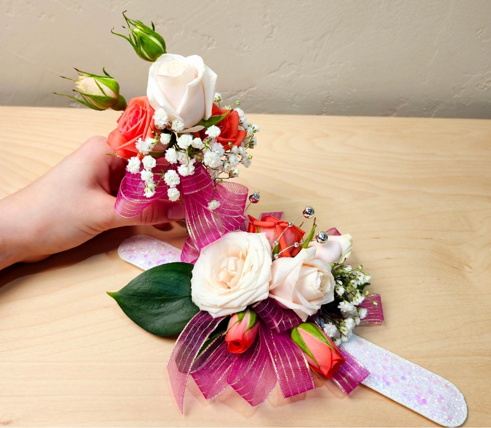 A corsage and boutonnière featuring an arrangement of flowers on a ribbon, held in one hand against a wooden surface.
