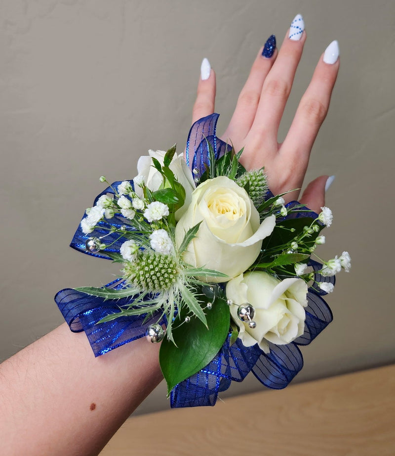 Hand wearing a wrist corsage with flowers against a plain background